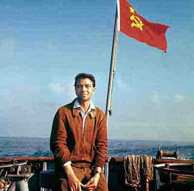 Peter Bock-Schroeder, Soviet Union 1956 German Photo Journalist relaxes on a boat on the black sea, with a bold red soviet flag fluttering behind him, enhancing the scene's nautical atmosphere.